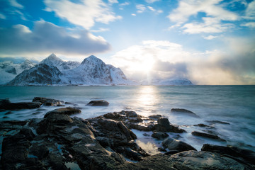 Fototapeta na wymiar Sunrise on the stone shore of the ocean and mountains with snow on the horizon