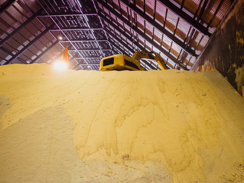 Backhoe handling raw sugar bulk store in bulk warehouse.