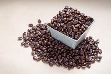 roasted coffee beans in square galvanized iron bucket and heap on space of brown paper