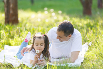 Young father and daughter lying on green grass. Happy daughter sitting on father back and smiling. looking up