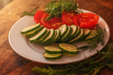 Rural still life: fresh sliced tomato and cucumber, parsley and dill on a plate on the old table.