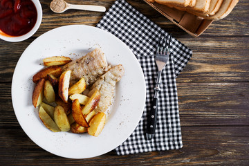 Delicious dinner, fast food, a national dish, fish with fried potatoes, fish and chips, sauce and white toast bread on a dark wooden background 