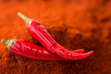 chili red hot pepper, concept of popular spice - closeup on two delicious juicy pods of red chili pepper isolated over the top of red curry powder, top view, flat lay, selective focus