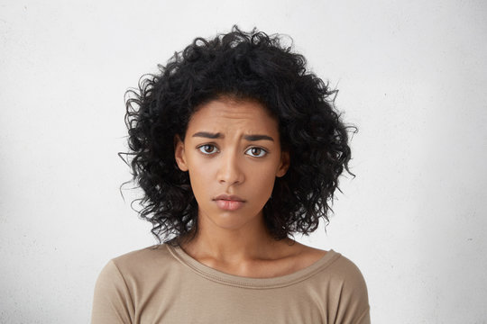 Headshot of regretful young mixed race woman feeling sorry for doing something wrong, looking at camera with brows frowned, doing her best to get forgiveness from her boyfriend during quarrel