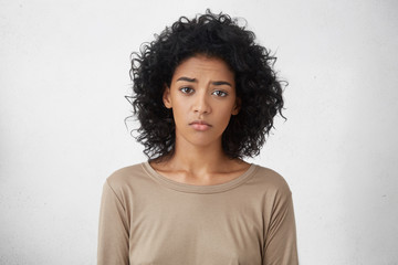 Attractive upset young dark skinned lady with Afro hairstyle feeling sad or bored expression while spending weekend at home, looking unhappy after friends forgot to invite her to party. Horizontal - obrazy, fototapety, plakaty