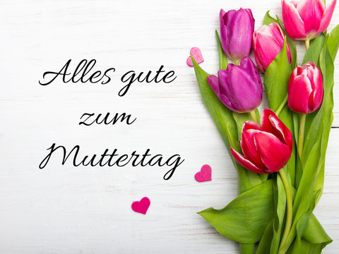 German Mother's day card with word Muttertag (Mother's day) tulip and hearts on white wooden background.