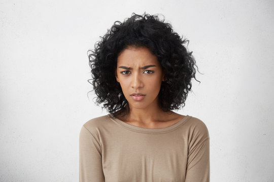 Human facial expressions, emotions, feelings and life perception. Good looking young dark-skinned woman with pretty face and dark clean skin having uncertain and frustrated look, posing indoors