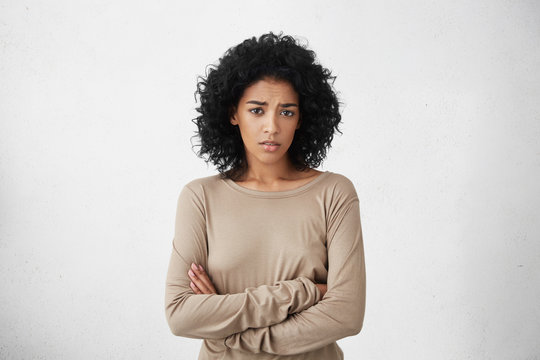 Indoor shot of skeptical young mixed race woman feeling suspicious, her look expressing disapproval or doubt, keeping arms crossed while having a suspicion that her husband cheated on her. Horizontal
