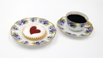 Pastry cookie with a red jam heart and icing powder sugar - Vintage bone china porcelain with flower pattern, pansy viola, golden brim - Plate, coffee cup - Isoalted, white background, copy text space