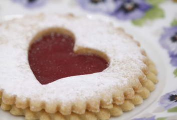 Pastry cookie with a red jam heart and icing powder sugar - Vintage bone china porcelain with flower pattern, pansy viola, golden brim - Plate, coffee cup - Isoalted, white background, copy text space