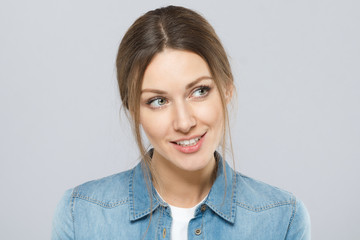 Indoor closeup of attractive female isolated on gray background looking rightwards with happy interested smile and big green eyes showing attention, curiousity and wiilingness to learn secret.