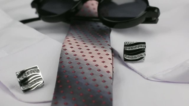 Red tie, cufflink and sunglasses on a white shirt, close-up. Dolly shot.