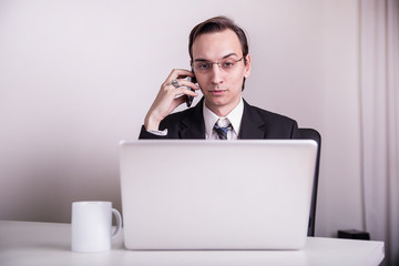 Young business man drinking coffee and talking on a cell phone in the office
