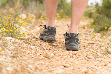 Foto a nivel del suelo de botas de montaña sobre un camino de tierra rodeado de flores amarillas	