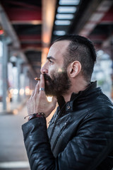 A portrait of a tough, bearded man lighting a cigarette in the streets of Brooklyn, New York City. Sitting on the subway stairs, lit by a light overhead. Shot during the Spring of 2017.