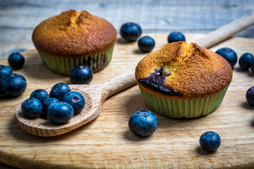 Blueberry muffin and blueberries on a wooden spoon on wooden background