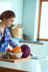 Obraz na płótnie Canvas Young woman cutting vegetables in kitchen near desk