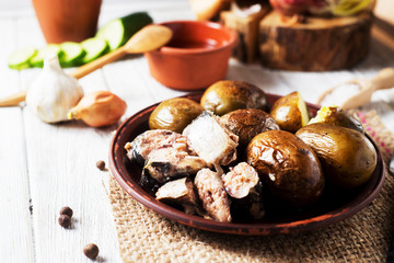Russian and Ukrainian national cuisine, potatoes in their skin with fish, white bread, onions, garlic, cucumber and vegetable oil on a light wooden background 