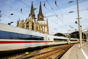 Zug fährt durch Kölner Bahnhof mit Dom im Hintergrund