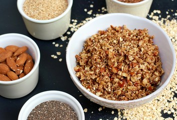 Homemade granola in white bowl with almond and seeds on black background