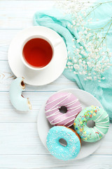 Tasty donuts with sprinkles and cup of tea on wooden table