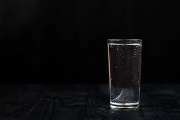 Fotobehang Gewoon een glas water op een zwarte achtergrond. Mineraalwater in een glas op een donkere houten tafel. © ptizza_dodo