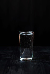 Just a glass of water on a black background. Mineral water in a glass on a dark wooden table.