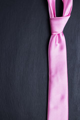 Pink elegant tie on black textured background.