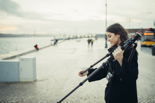 Young enthusiastic female photographer setting up lightweight carbon travel tripod for sunset/sunrise log exposure still shot.Stabilized photography and video.Equipment for outdoor landscape filming.