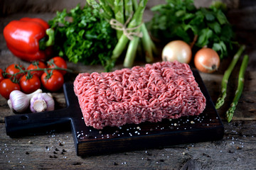 Fresh raw ground beef with fresh vegetables on an old wooden background. Rustic style.