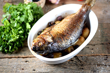 Baked golden fish with carp with potatoes and mushrooms on an old wooden background. Rustic style.