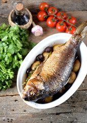 Baked golden fish with carp with potatoes and mushrooms on an old wooden background. Rustic style.