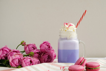 Purple coffee in stylized mason jar cup with macarons and roses and colorful decoration. Blueberry milk shake. Unicorn coffee. Unicorn food