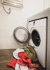 Washing machine with multicolored dirty towels on the floor near it. laundry washer with opened door. Side view. Vertical