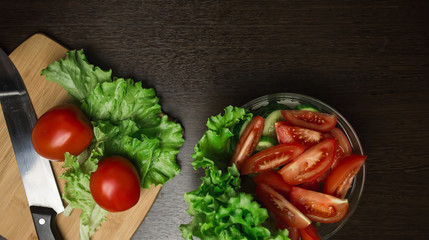 tomato and cut tomato, cucumber and a kitchen knife on a cutting board