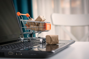 Online shopping concept. Shopping cart, small boxes, laptop on the desk