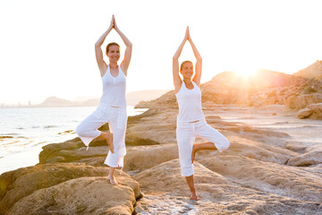 Two sisters are doing yoga exercises at the seashore of Mediterranean sea