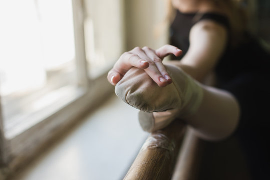 Young beautiful ballerina warming up in ballet class. Close up, girl in black leotard stretch at ballet class stretching muscles at the barre. Focus on the leg - Powered by Adobe