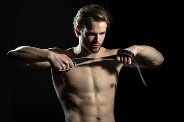 Belt is in the hands of naked man. The guy does exercises for hands with leather belt. Sexy model for men's accessories. Concentration and meditation in the gym