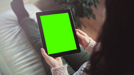 Indoor shot of a woman using tablet pc with green screen sitting on white sofa, vertical orientation