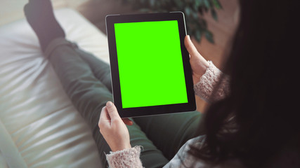 Indoor shot of a woman using tablet pc with green screen sitting on white sofa, vertical orientation