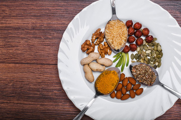 Assorted nuts in white bowl, plate on wooden surface.  peanuts, almonds, hazelnuts, pumpkin seeds, walnuts, rice , buckwheat. Top view with copy space