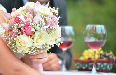 Bride holding a bouquet of flowers, with glasses of wine in the background