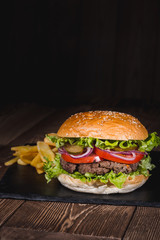 Fresh burger in bun with sesame with lettuce, tomato, beef and onion on wooden table.