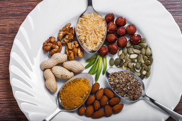 Assorted nuts in white bowl, plate on wooden surface.  peanuts, almonds, hazelnuts, pumpkin seeds, walnuts, rice , buckwheat. Top view with copy space