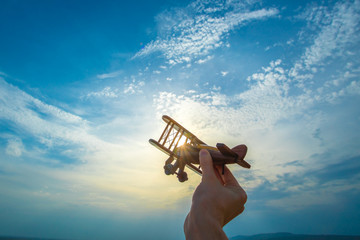 The hand with a wooden airplane on the blue sky background