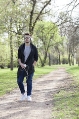 Young man walks in the park, holding the phone in his hand and listen to music