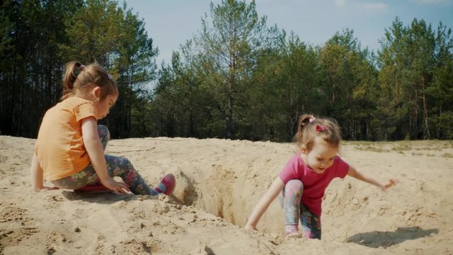 Two lovely girls play on the sand in the woods in the summer