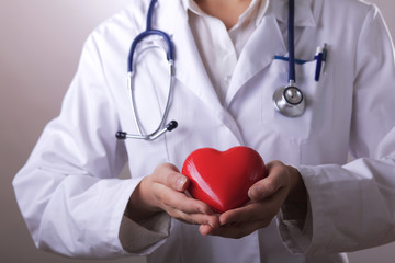 Female doctor with stethoscope holding heart,on dark background