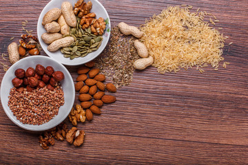 Assorted nuts in white bowl, plate on wooden surface. Top view with copy space